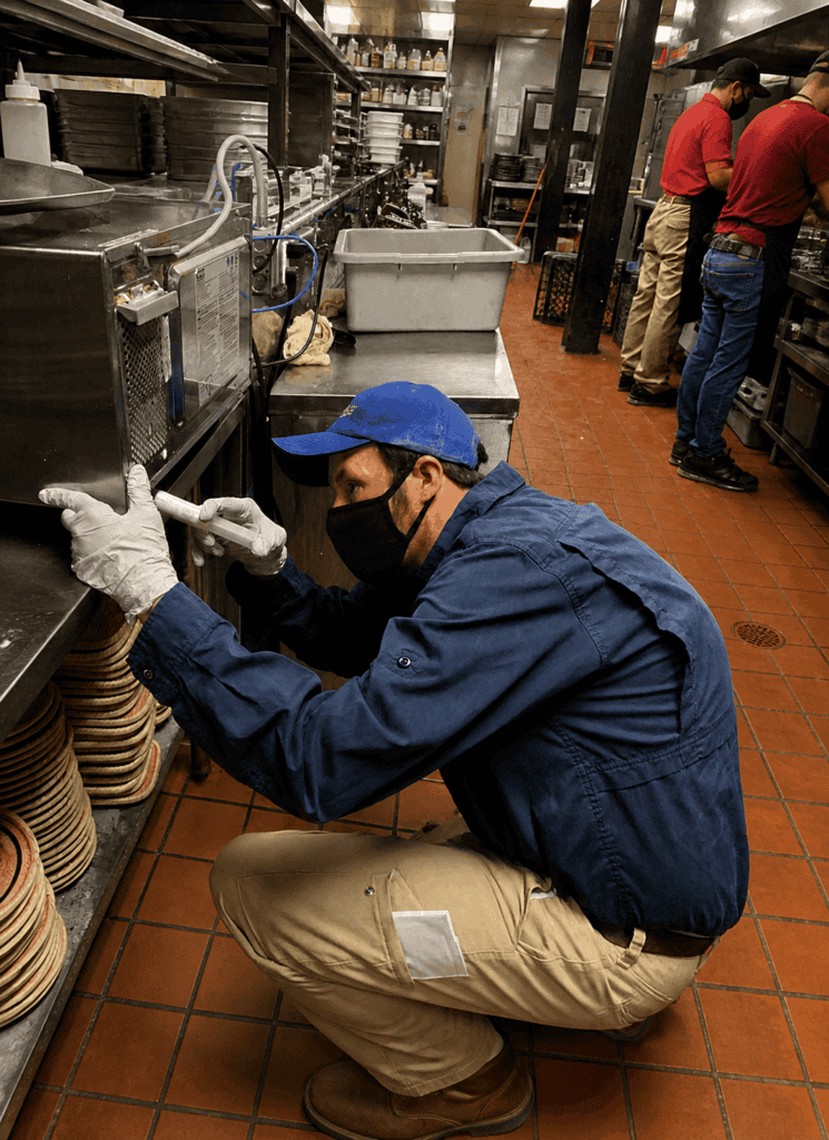 Commercial pest control technician inspecting equipment in a restaurant kitchen